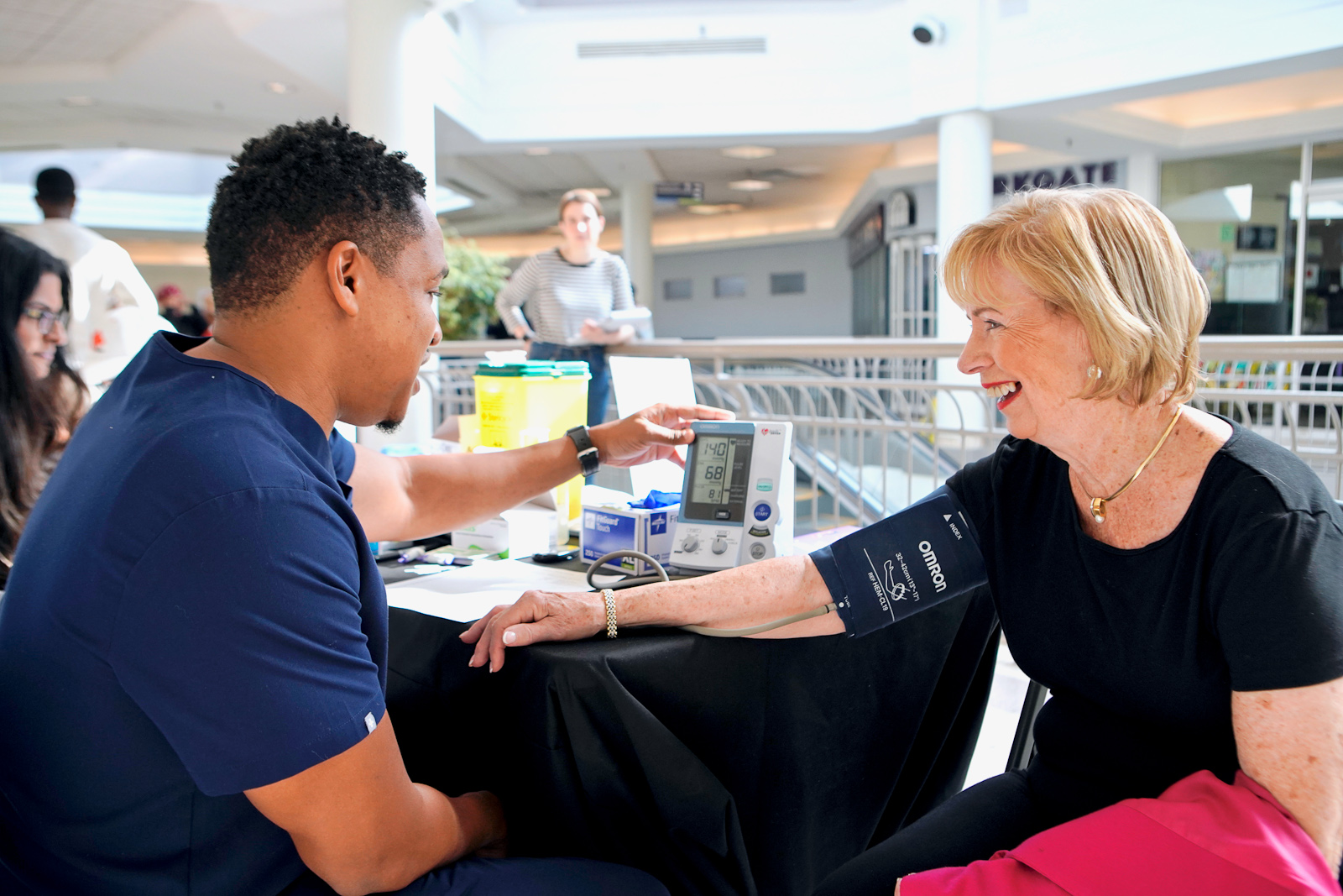 A clinician is measuring a person's blook pressure at an information table in a mall. 